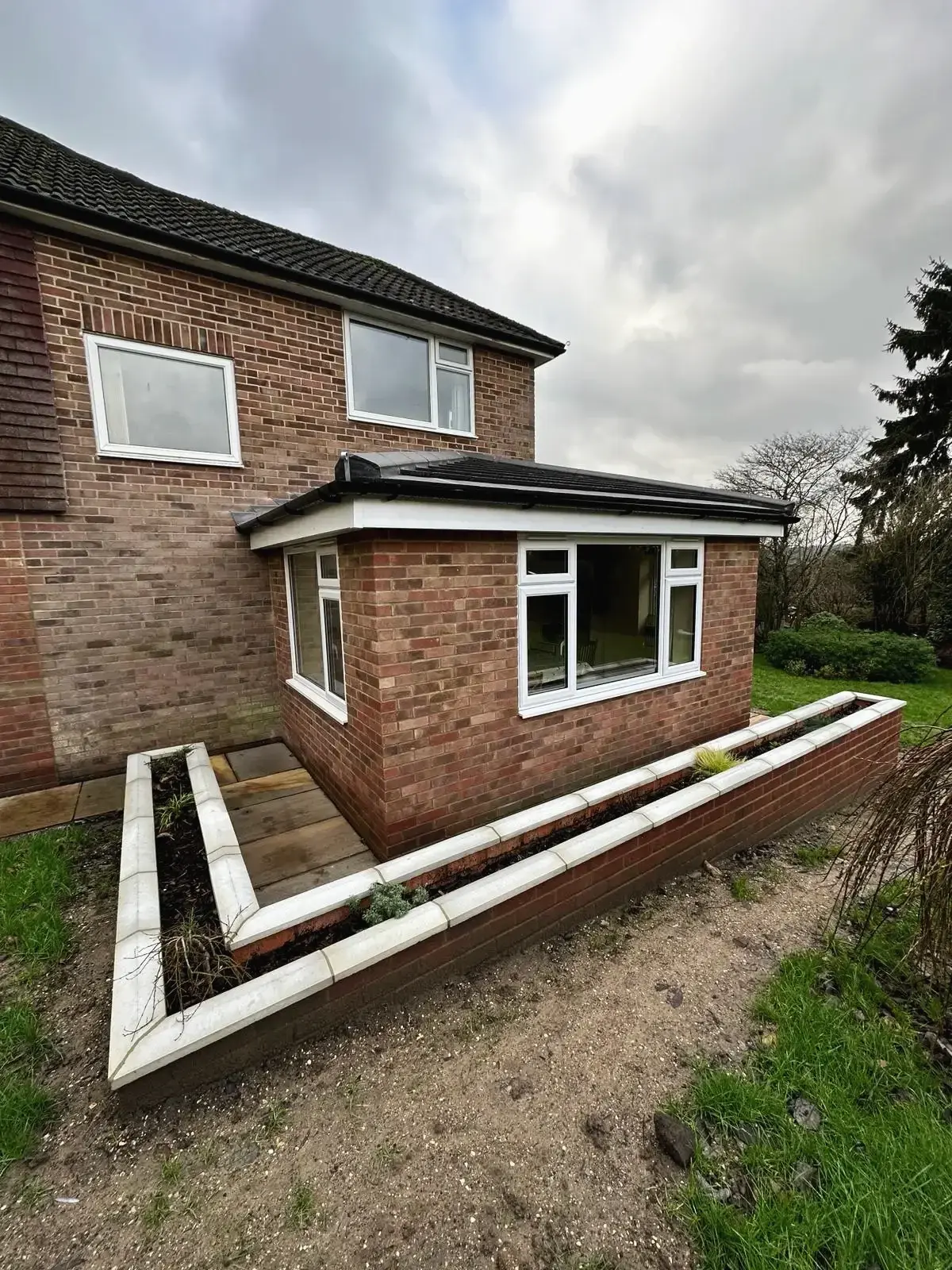 Single-storey brick extension with white windows and a tiled roof above a new planter wall