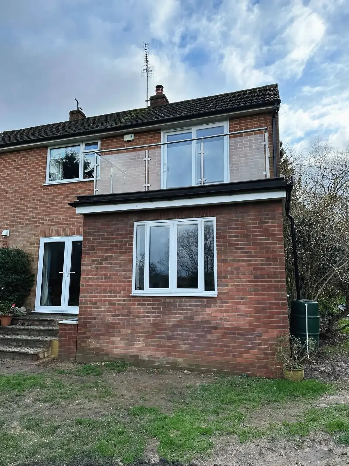Two-storey brick extension with French doors below and a glass balustrade above