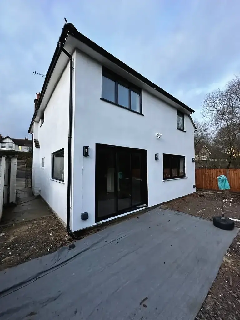 Two-storey extension finished in white render, with black-framed glazing and wall lights